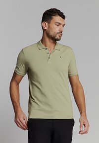 Olijfgroene poloshirt van gestructureerde katoen met een klassieke kraag, twee knopen en een klein logo accent op de borst.
