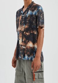 Kurzarm-Hemd mit Knopfleiste im schwarz-braun-blauen Batikmuster; aus einem leichten Stoff gefertigt; lockere Passform mit Camp-Kragen.