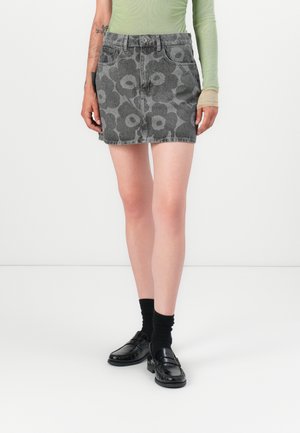 Denim mini skirt in grey with floral pattern, five pockets, and metal button. Paired with black socks and shoes.