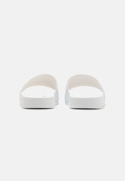 Sandales blanches à glissement avec un design minimaliste, dessus lisse et semelle en caoutchouc texturé. Dos ouvert et large sangle pour plus de confort.
