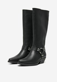 Bottes noires en cuir hautes jusqu'au genou avec un bout pointu, présentant une fermeture éclair sur le côté et une sangle décorative avec des accents en métal argenté.