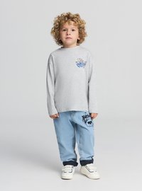 Szara koszula z długim rękawem z niebieskim motylem; jasnoniebieskie spodnie z czarnym nadrukiem; białe trampki na rzepy.