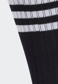 Calcetín deportivo a rayas negro y blanco con textura acanalada y diseño hasta la rodilla, con múltiples rayas horizontales blancas.