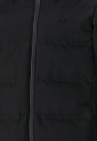 Sort puffjakke med en glat overflade, der har en frontlynlås og diskret branding. Designet har en quiltet struktur og minimale sømme.