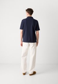 Polo shirt in cotone navy a maniche corte, orlo dritto e colletto classico, abbinato a pantaloni bianchi a gamba larga e mocassini marroni.