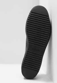 Semelle de chaussures Clarks noire avec une surface texturée, comportant des rainures horizontales et un bord lisse et arrondi. Le logo est embossé près du talon.