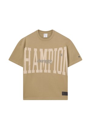 T-shirt beige oversize Champion con grande scritta pallida "CHAMPION" sul fronte e logo più piccolo sulla manica, collo rotondo e maniche corte.
