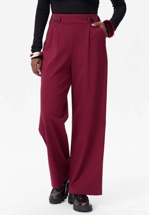 Pantalons larges bordeaux à taille haute, dotés de deux boutons à l'avant et de poches latérales. Fabriqués dans un tissu lisse avec une coupe ajustée.