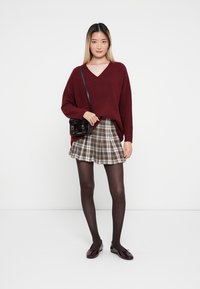 Bordeaux oversized gebreide trui, geruite flared rok, zwarte handtas, donkere panty’s en glanzende bordeaux platte schoenen. Geven een textuur patroon op de kleding.