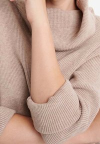 Ljusbeige stickad tröja med polokrage och ribbad struktur. Ärmarna är uppkavlade, vilket visar mjukt tyg och en avslappnad passform.