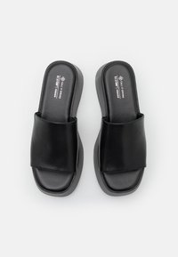 Sorte veganske slidesandaler med en bred stropp over foten og en blokkhel. Myk tekstur og glatt finish fremhever et minimalistisk design.