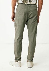 Grüne, schmal geschnittene Hosen mit einer glatten Textur. Verfügen über zwei Gesäßtaschen und hochgekrempelte Säume, kombiniert mit weißen Sneakers.