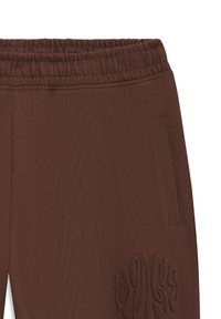 Brune joggingbukser med ribbet struktur, elastisk taljebånd og sidelomme med en markant skulptureret logodetalje.