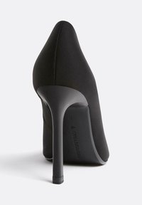 Scarpa nera con tacco alto, punta affusolata, design elegante, texture liscia e tacco a stiletto sottile. Logo del marchio visibile sulla suola.