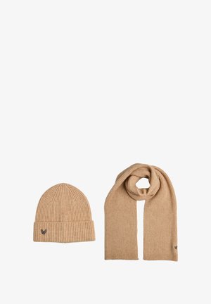 Bonnet beige en tricot avec revers retourné et détail brodé, assorti à une longue écharpe beige côtelée, tous deux en tissu doux et texturé.