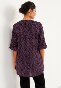 Lange paarse top met een geometrisch bladerenpatroon, driekwart mouwen en een relaxte pasvorm. Soepele textuur met een ronde halslijn.