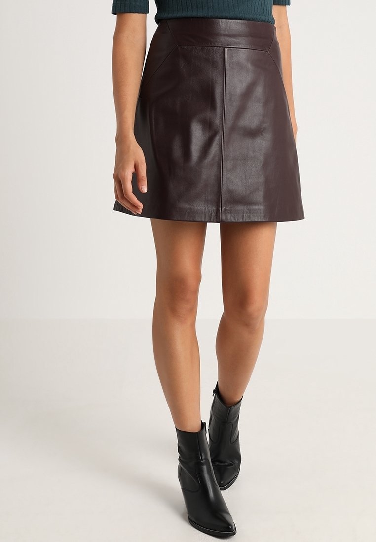 Burgunderrote Leder-Minirock mit einer glatten Textur, mit einem taillierten Bund und dezenten Steppnähten. Kombiniert mit schwarzen Stiefeletten.