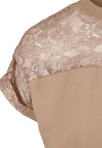 Beige Oberteil mit kurzen Ärmeln und zarter Spitzenbedeckung im floralem Muster. Weiche Textur mit rundem Ausschnitt und dezentem Glanz.