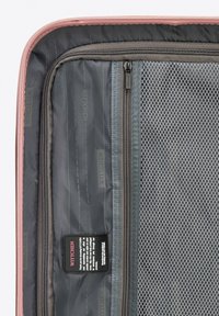 Innenansicht eines rosa Koffers mit Netzfächern, dunkelgrauem Stoff mit feinem Muster und einem Pflegeetikett an der Seite angenäht.