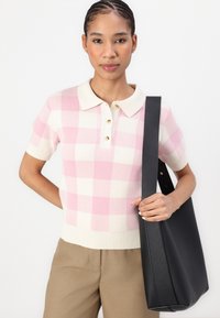Kortermet polo genser med et rosa og hvitt rutemønster, ribbet nederkant og tre gullknapper, kombinert med en svart tote-veske.