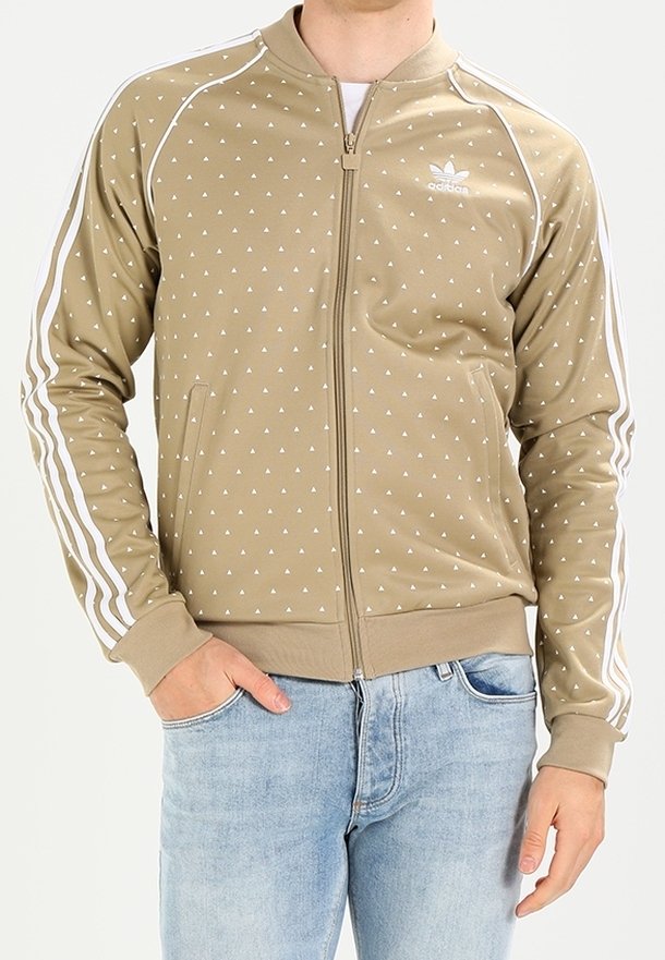 Beige zippered jacket with white triangular pattern, raglan sleeves, and white stripes along sides. Features Adidas logo on chest.