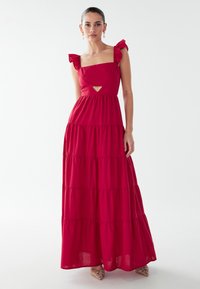 Vestido maxi rojo con volantes en las tiras de los hombros y escote cuadrado con abertura en forma de ojo de cerradura. Tela ligera con textura suave.