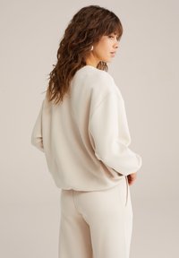 Felpa color crema con vestibilità ampia, spalle ribassate e fessure laterali. Tessuto morbido e liscio con un design minimalista.