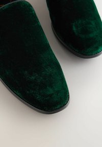 Green velvet slip-on shoes with a smooth texture and pointed toe. Features a sleek black sole and a glossy finish.