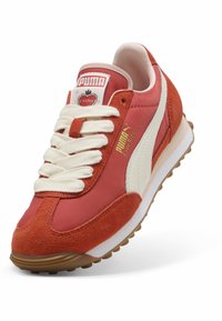 A PUMA Easy Rider sportcipők vörös velúrból és textilből készült felsőrésszel rendelkeznek, krémszínű fűzőkkel, fehér oldalsávval és struktúrált gumi talppal.
