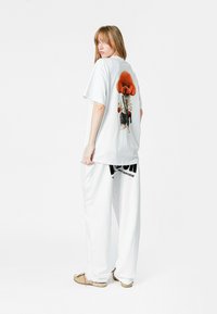 Camiseta blanca de gran tamaño con un gráfico de un perro en la parte de atrás. Combinada con pantalones blancos sueltos. El conjunto tiene un ajuste relajado y un estilo casual.