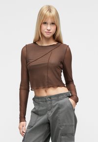 Καφέ διαφανές crop τοπ με μακριά μανίκια, γεωμετρικό σχέδιο και στρογγυλή λαιμόκοψη, σε συνδυασμό με γκρι cargo παντελόνι με τσέπες.