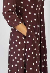 Brązowa sukienka w białe kropki, z rękawami do połowy przedramienia i luźnym krojem, z bocznymi kieszeniami i gładką fakturą tkaniny.