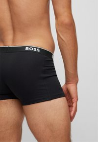 Boxeri negri, cu un design ajustat, dintr-o țesătură moale, având un brâu contrastant cu logo-ul "BOSS" în alb.