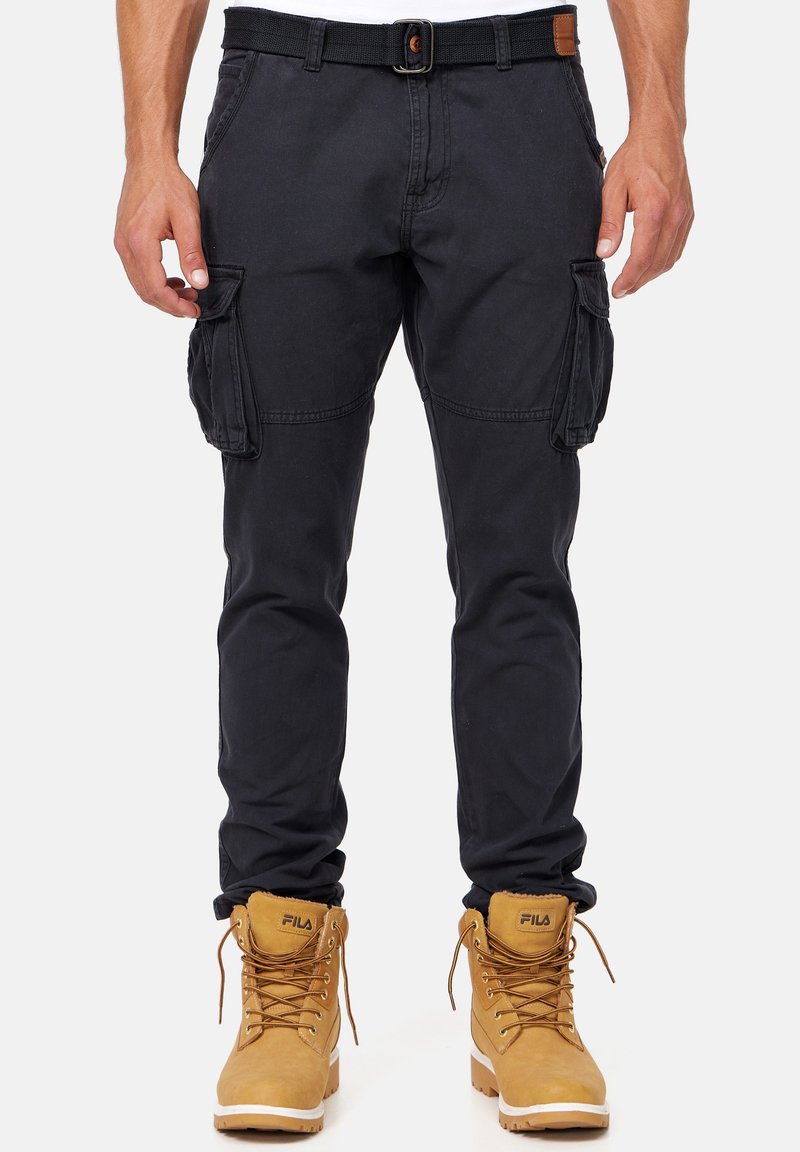 Pantalones cargo azul marino con múltiples bolsillos laterales, presillas para cinturón y un corte ajustado, combinados con botas color beige que presentan cordones marrones y detalles con el logotipo.