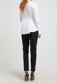 Blouse blanche à basque avec un corsage ajusté et un ourlet évasé, associée à un pantalon noir slim et des sandales à talons noires.