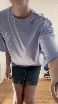T-shirt oversize bluastro chiaro con grafica a onda, abbinato a una gonna di jeans scuri con chiusura a bottoni e orlo sfilacciato.