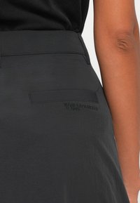 Crna suknja s teksturiranom površinom, s stražnjim džepom i utisnutim logom "KARL LAGERFELD JEANS". Glatka tkanina i minimalistički dizajn.