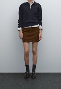 Marinblå zip-up-tröja, vit skjorta under, brun mocka minikjol, mörkgrå strumpor och svarta snörskor.