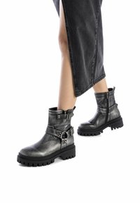 Botas de tobillo de cuero negro con acabado texturizado, hebillas ajustables y una suela de goma gruesa. Cierre con cremallera lateral.