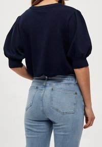 Mörkblå puffärmad tröja med ribbad krage och manschetter, kombinerad med ljusblå tajta jeans med bakfickor och metallnitar.