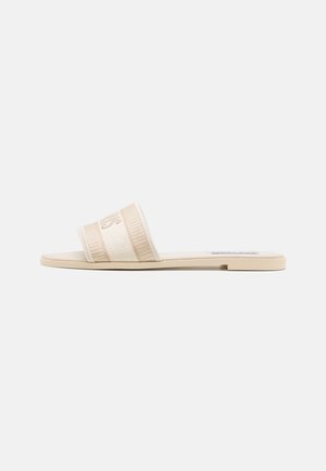 Sandale plate beige avec une large bride en tissu et un petit talon, vue de côté sur fond blanc.