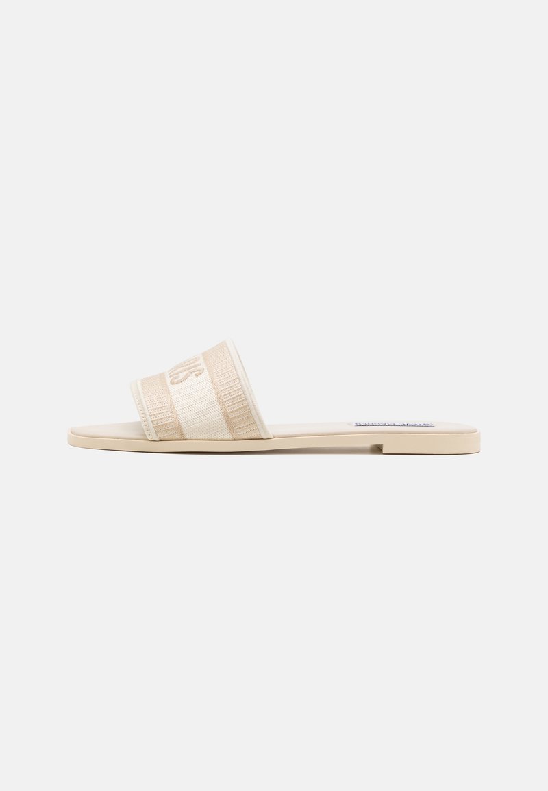 Sandale plate beige avec une large bride en tissu et un petit talon, vue de côté sur fond blanc.