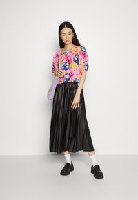 Top floral de mangas curtas em rosa, amarelo e azul; combinado com uma saia maxi plissada preta; bolsa retangular roxa; sapatos plataforma pretos.