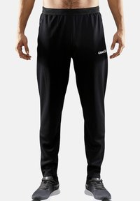 Sorte træningsbukser lavet af et glat, letvægtsmateriale. Har en elastisk talje og et logo-detail på venstre lår.