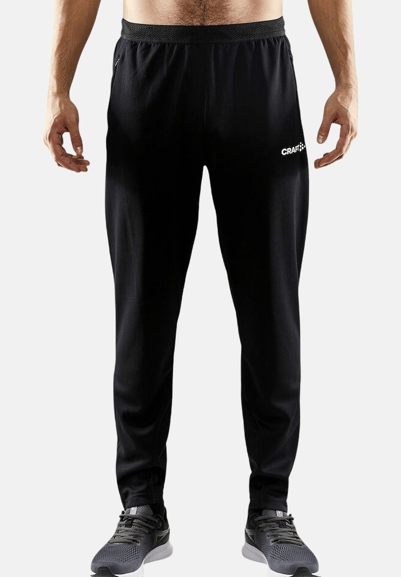 Sorte træningsbukser lavet af et glat, letvægtsmateriale. Har en elastisk talje og et logo-detail på venstre lår.