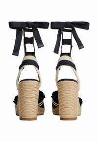 Espadrille heels with woven jute base, navy canvas straps, and a textured pom-pom accent. Features ankle ties and an open-back design.