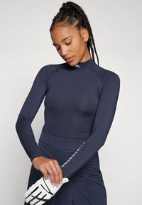 Tengerészeti kék hosszú ujjú sportfelső, rugalmas anyagból készült, magas gallérral, slim fit fazonnal és fehér logó részlettel a csuklón.