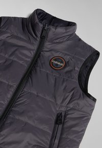 Gilet rembourré gris foncé, avec un col haut, une fermeture éclair intégrale et une patch logo. Texture lisse avec un design matelassé horizontal et une poche latérale.