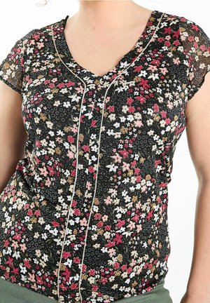 Donna che indossa una blusa nera a scollo a V con motivo floreale rosso, bianco e marrone e maniche corte di tessuto trasparente su sfondo bianco.