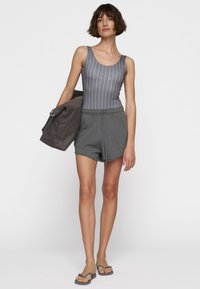 Traje de baño de una pieza a rayas grises con logo, combinado con pantalones cortos grises con cintura ajustable y chanclas. Tela suave, diseño casual.